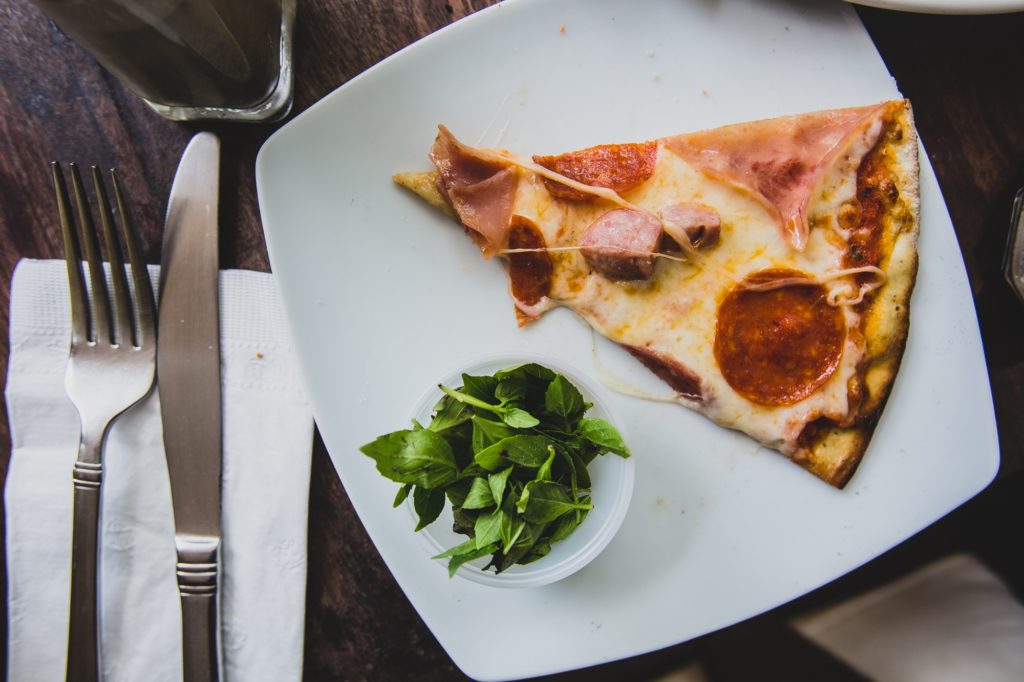 piece of pizza on a plate with green herbs
