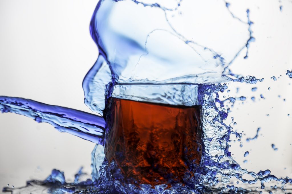 red glass of soda with blue water splashing onto it